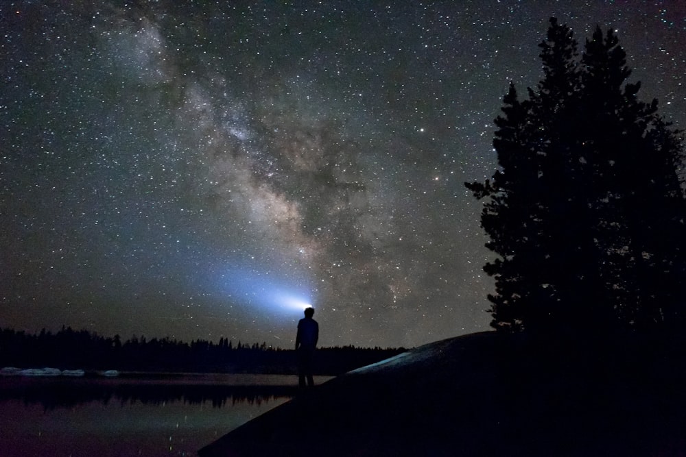 Silhouette d’homme debout près du plan d’eau sous le ciel nocturne