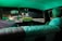 Inside the vintage car, two people are seated, one person visible from the back and another in the rearview mirror. The dashboard features a prominent 'TAXI' sign and the interior is lit with a green glow. The road ahead is dimly lit, with streetlights illuminating the night scene.