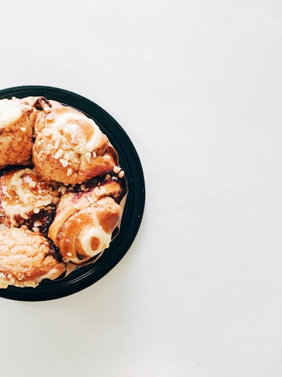 An assortment of colorful, flaky pastries arranged on a white ceramic plate with a cup of coffee in the background