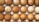 A collection of eggs arranged neatly in a carton, showcasing a variety of brown shades. The surface of some eggs is smooth while others have slight imperfections or speckles. The eggs are aligned in even rows, and the carton provides a textured background.