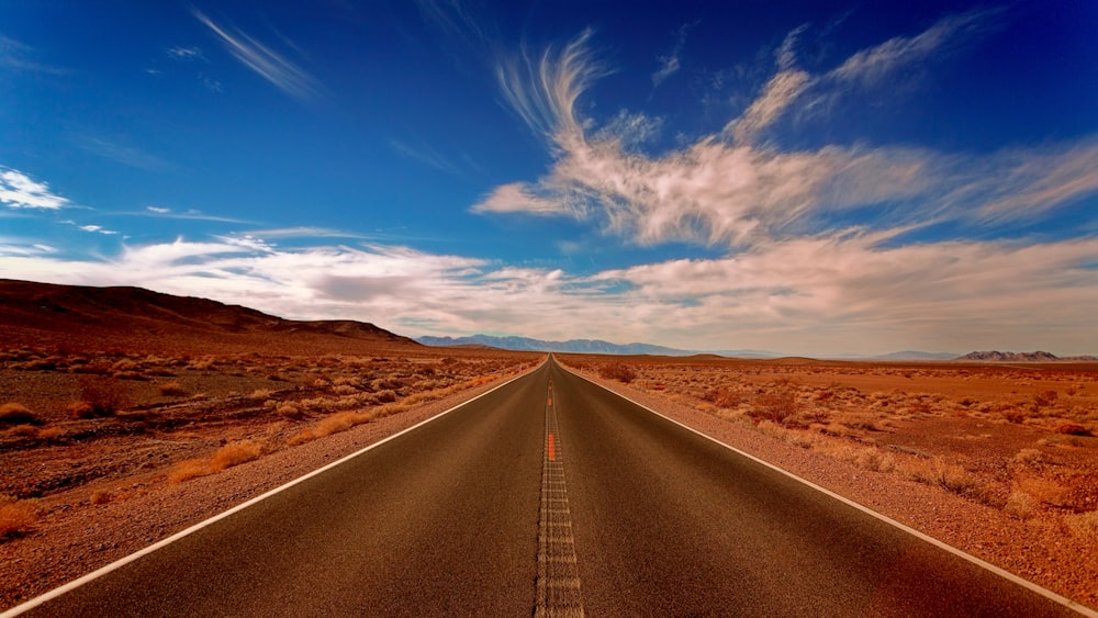 clear black concrete road under white and blue skies