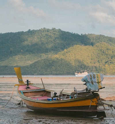 orange boat on seashore during daytime across mountain