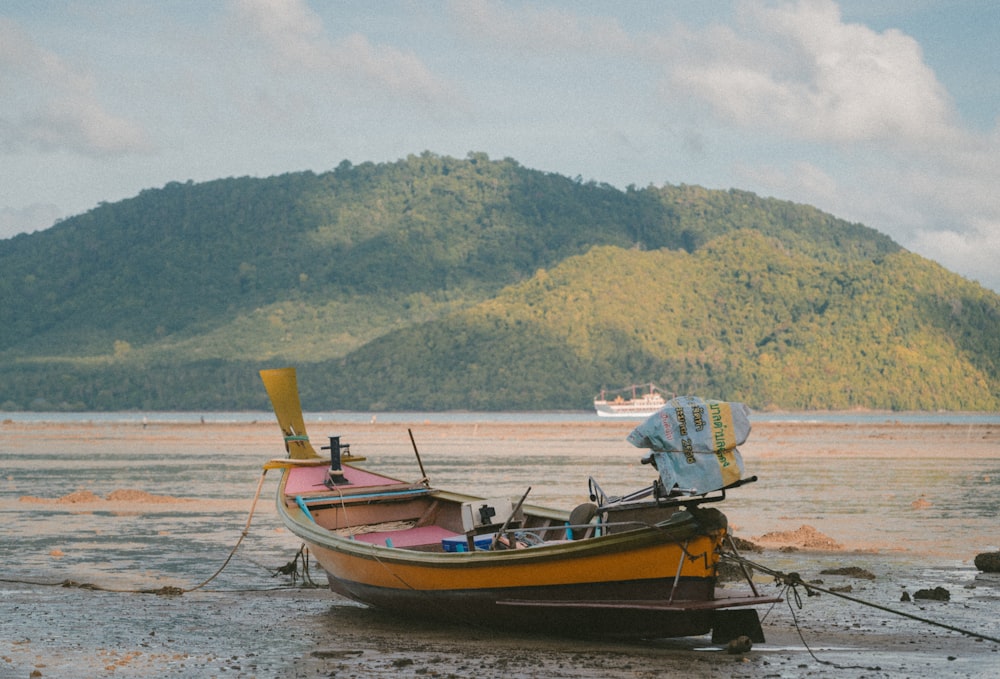 orange boat on seashore during daytime across mountain