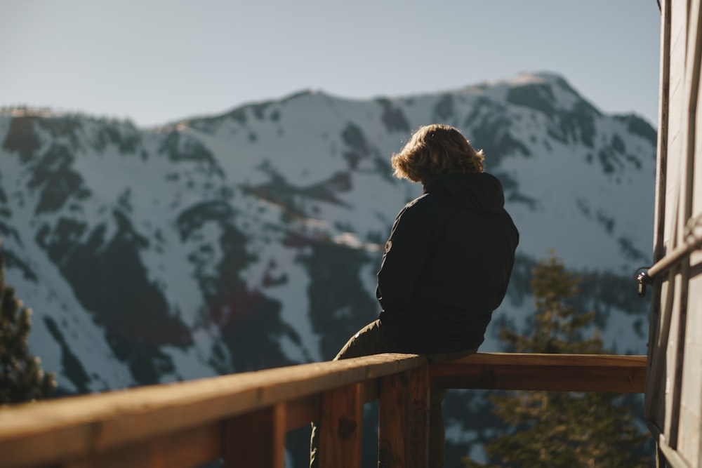 man sitting on balcony overlooking snow capped mountain