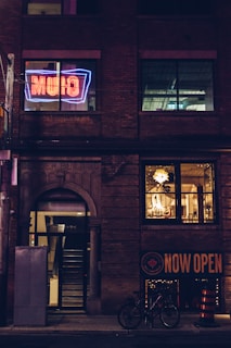 A vibrant storefront sign glowing warmly in the evening light on a busy Calgary street.