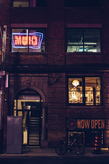 A vibrant storefront sign glowing warmly in the evening light on a busy Calgary street.