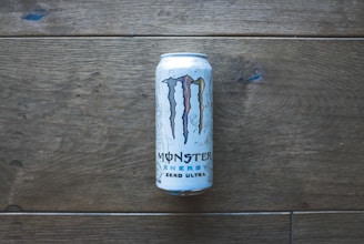 A can of Monster Energy Zero Ultra is placed vertically on a wooden surface. The can displays the iconic 'M' logo and has a minimalistic design with white and blue accents.