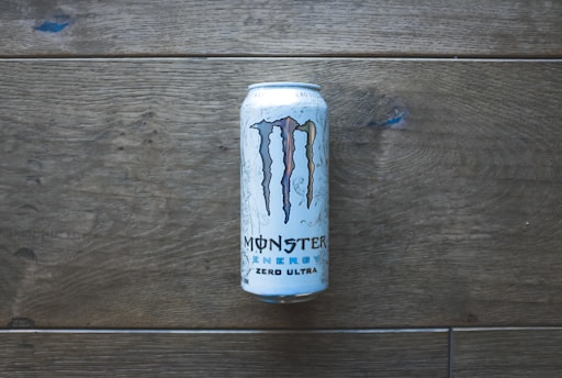 A can of Monster Energy Zero Ultra is placed vertically on a wooden surface. The can displays the iconic 'M' logo and has a minimalistic design with white and blue accents.
