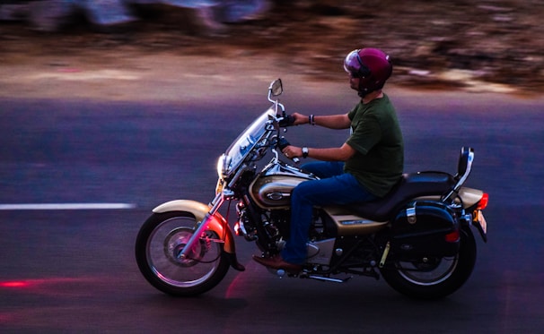 A rider preparing to start a classic motorcycle with a vintage helmet resting on the seat.