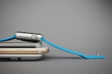 Two smartphones stacked on top of each other with a smartwatch resting diagonally on them. The smartwatch has a blue band and a metallic body.