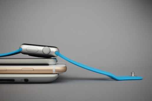 Two smartphones stacked on top of each other with a smartwatch resting diagonally on them. The smartwatch has a blue band and a metallic body.