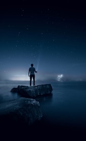 man holding flashlight standing on rock