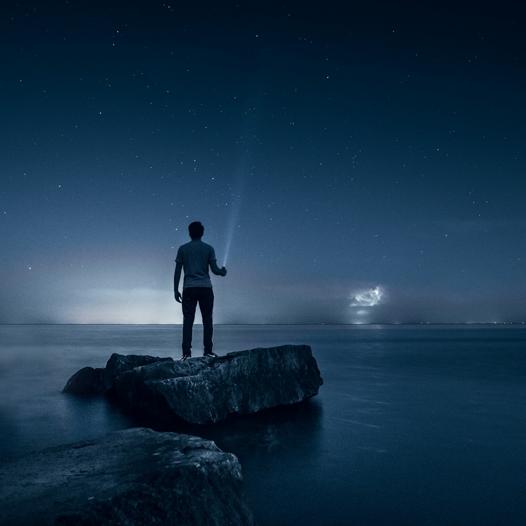 man holding flashlight standing on rock