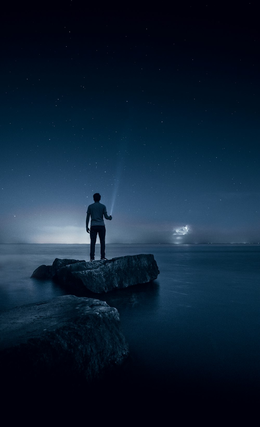 uomo che tiene torcia elettrica in piedi sulla roccia