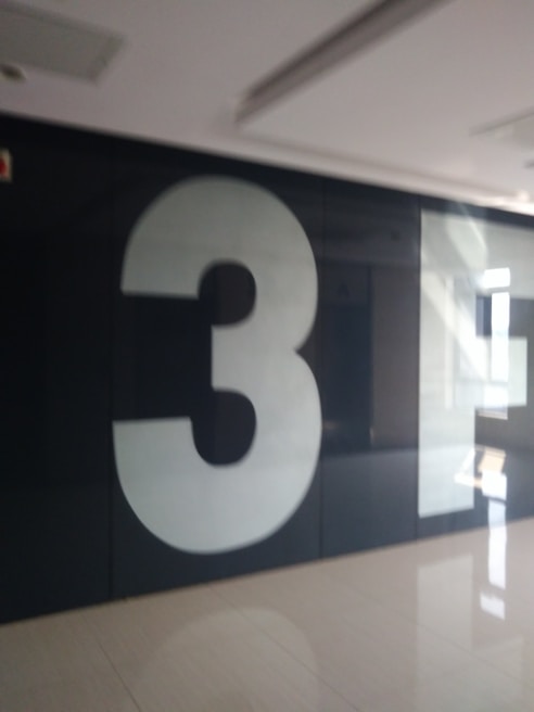 A large, white number three is prominently displayed on a dark wall in a hallway with a glossy floor reflecting light from windows.