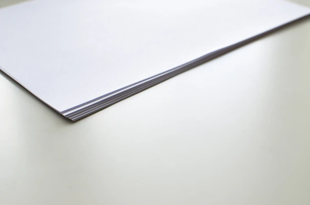 A neat stack of white paper sheets on a wooden table.
