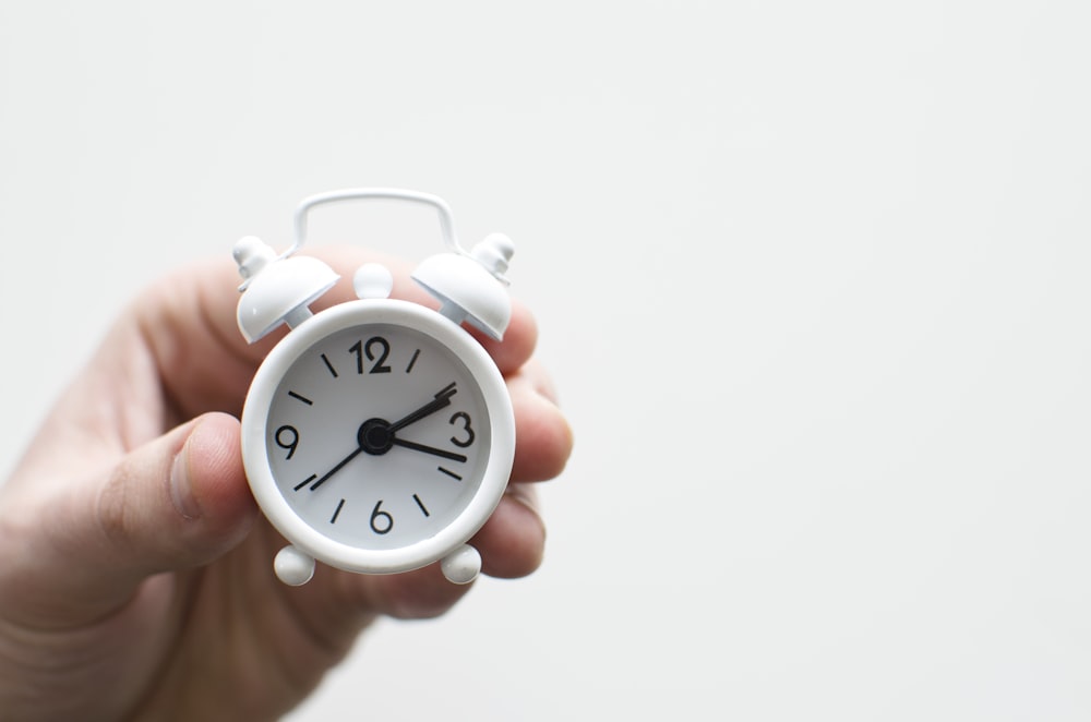 person holding white mini bell alarmclock