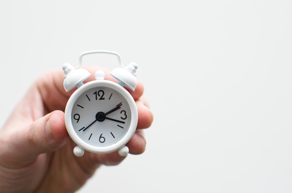 A hand holding a tiny white alarm clock