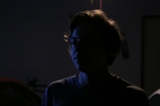 A silhouette of a person with soft, diffused lighting creating a halo effect around the edges of the hair. The background is dark, giving a mysterious and contemplative atmosphere.