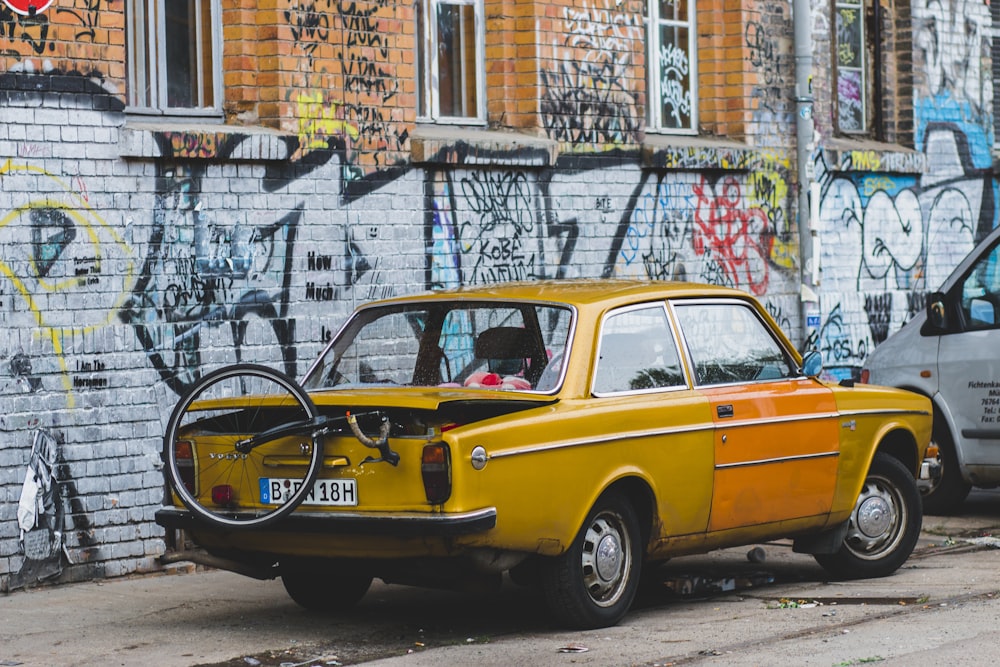 Coupé amarillo vintage con monociclo en el parque trasero cerca de la pared de graffiti