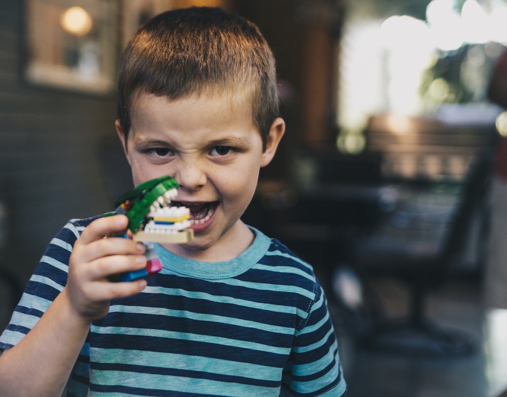 boy wearing teal and black striped t-shirt holding toy