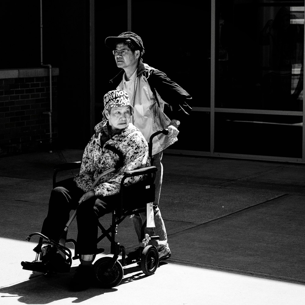 gray scale photo of man pushing wheelchair