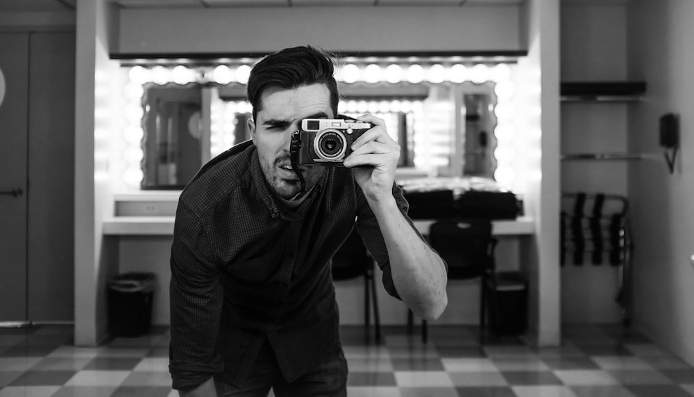 man holding camera bending down in grayscale photography