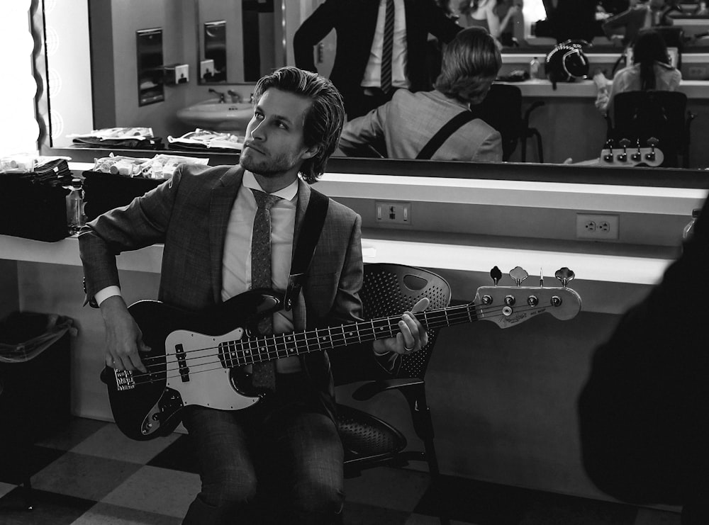 grayscale photography of man wearing suit holding guitar