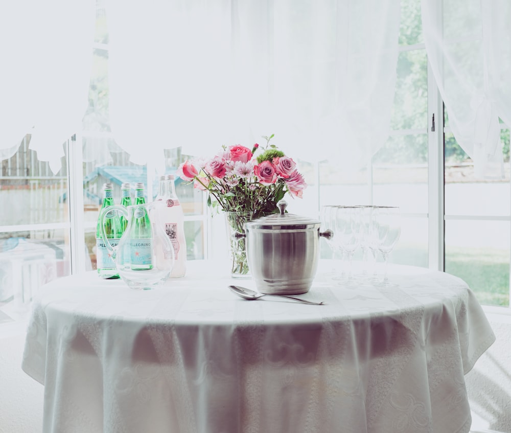 Centre de table fleur à pétales roses sur une table blanche à côté d’un récipient