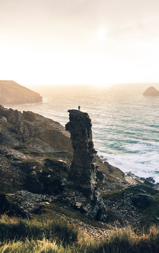 man standing on rock cliff near body of water in Tintagel United Kingdom