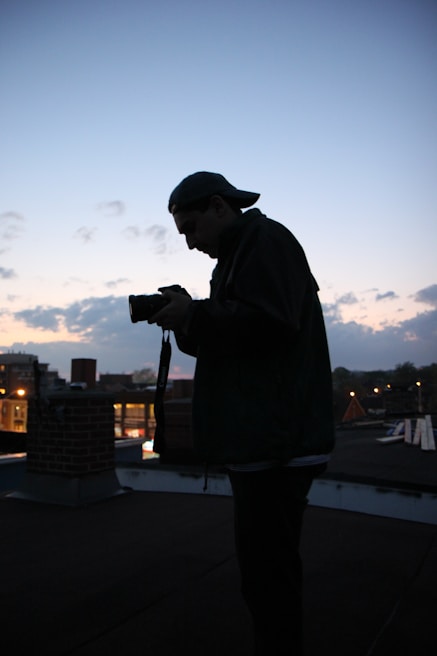 A silhouette of a filmmaker directing a scene during golden hour on an urban rooftop