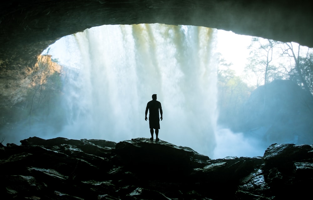 man standing on rock near cave