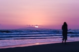 Sunset silhouette of a woman walking along the beach wearing a stylish, minimalistic bikini from Rosa Beachwear.