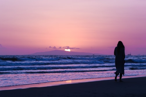 Romantic sunset silhouette of a white girl walking along the Goa shoreline.