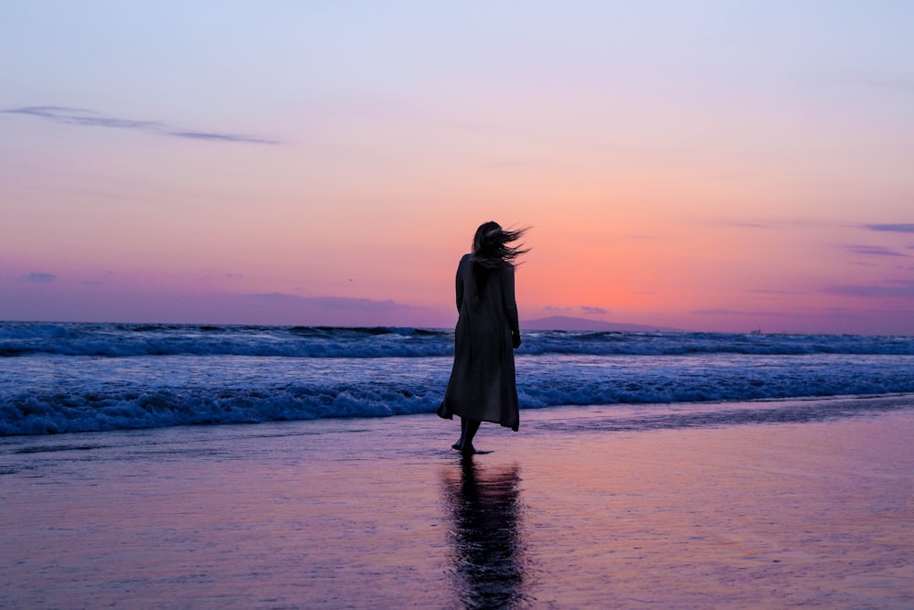mulher no vestido preto em pé na praia durante o pôr do sol