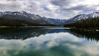 A serene lake reflecting snow-capped peaks surrounded by dense forests at dawn.