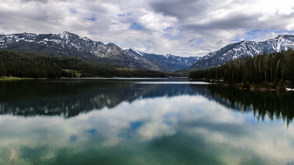 A serene lake reflecting snow-capped peaks surrounded by dense forests at dawn.