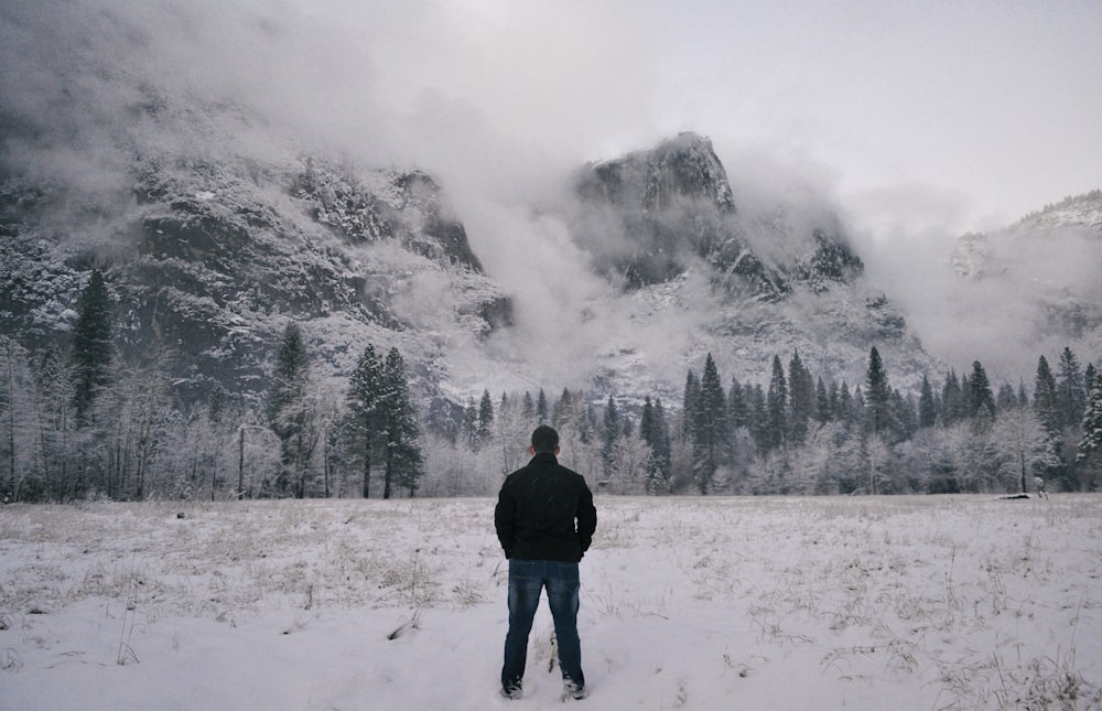 man in black jacket standing on snow covered ground