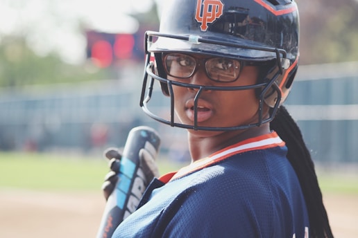 A close-up of a fastpitch softball player gripping a bat, with a blurred field in the background.