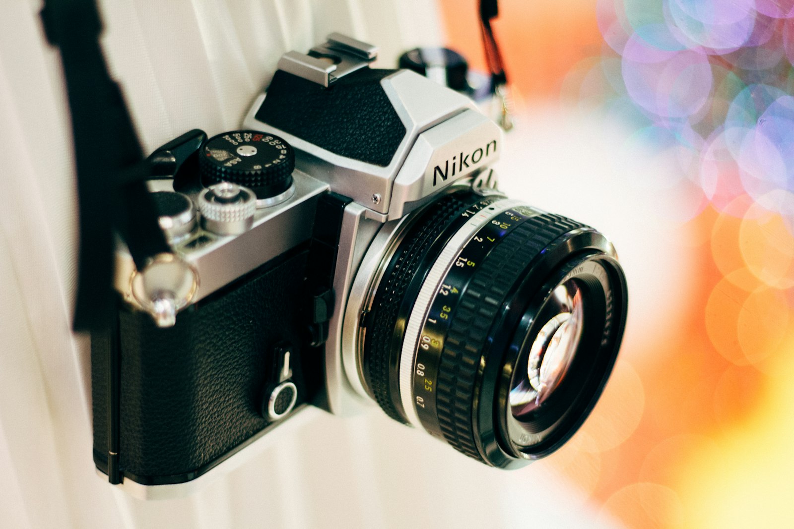 Renkli bokeh ışıklarından oluşan bir fon önünde prime lens takılı gümüş-siyah bir film fotoğraf makinesi