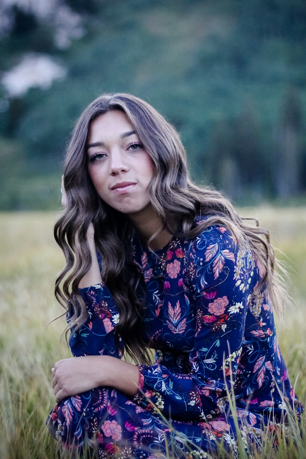 selective focus photo of woman sitting beside grass and wearing blue and white floral dress