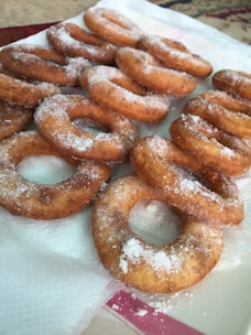 Several sugar-coated, fried doughnuts are arranged on a paper towel, displaying a golden-brown color and a light dusting of powdered sugar.