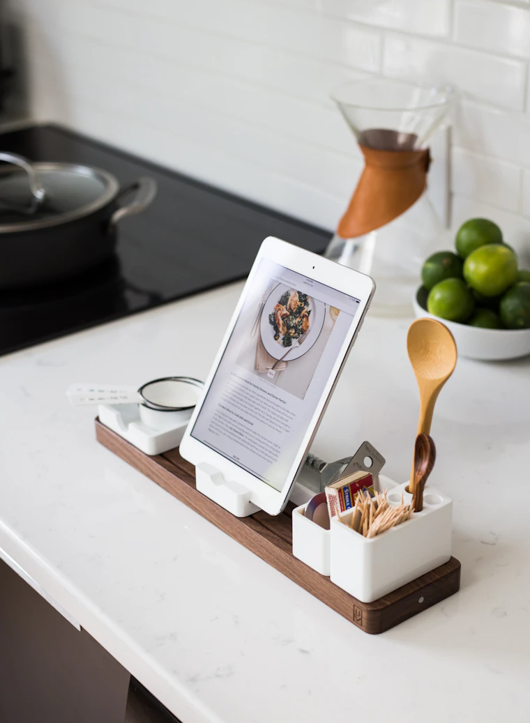 Mesón de cocina de mármol blanco con una tablet mostrando una receta, limones verdes y una cuchara de madera