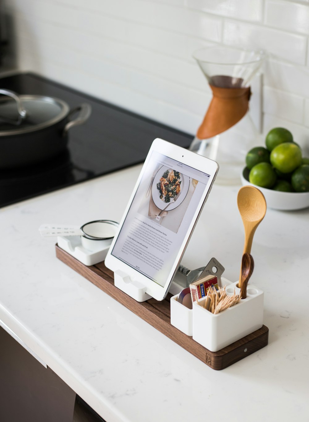 An iPad in a dock surrounded with kitchen utensils in a kitchen