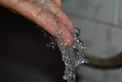 Close-up of clear water dripping from a tap into a hand, emphasizing clean water access.