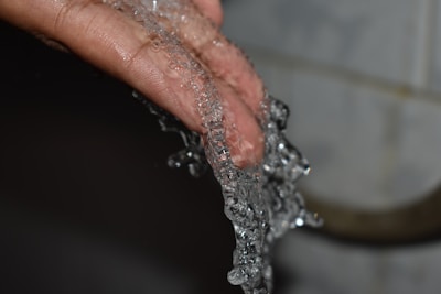 Close-up of water rinsing off debris from a grout brush's bristles under a kitchen faucet