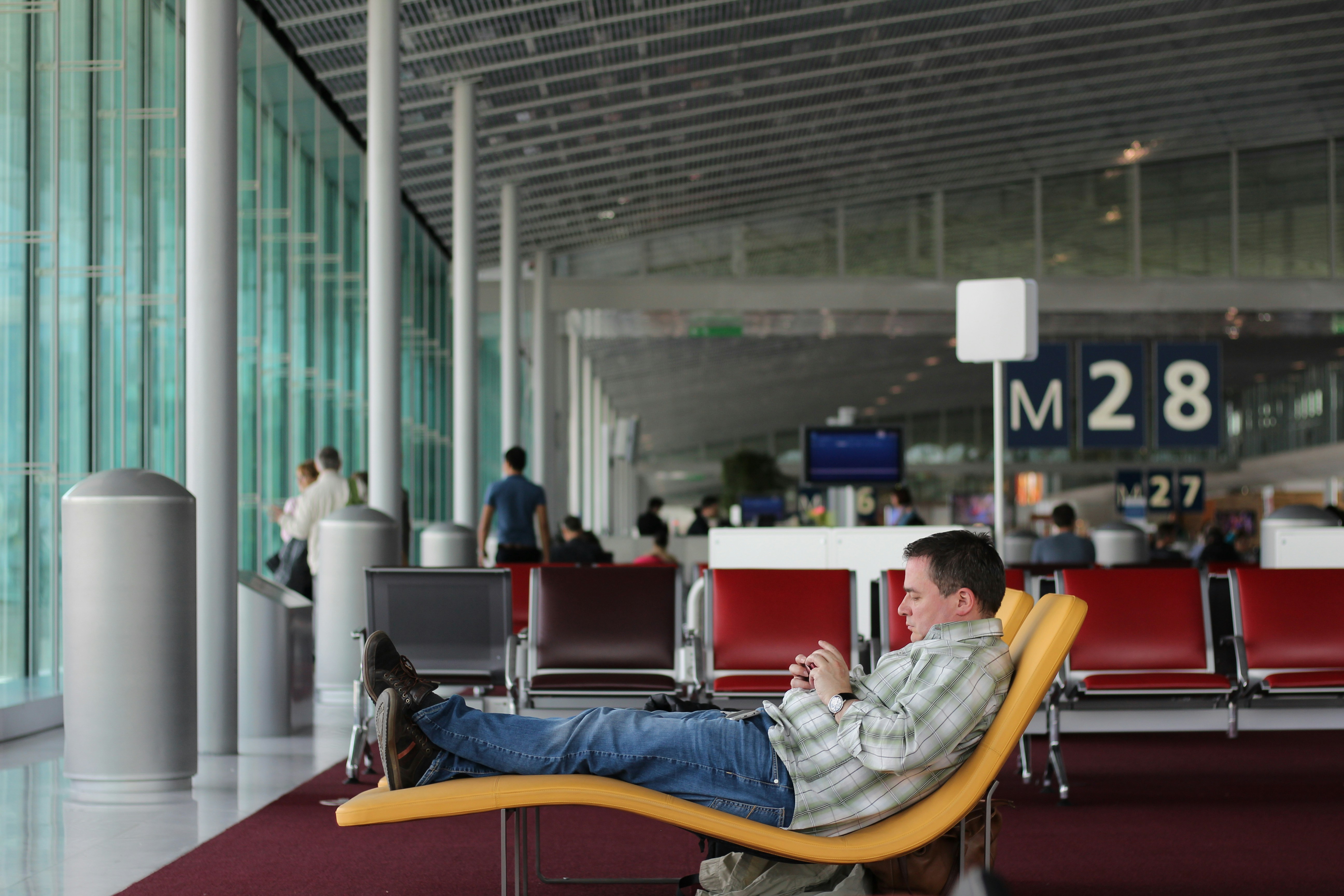 man sitting on airport waiting area, Part of traveling always involves waiting. In this case, while we waited at Gate 28 while our flight was boarding at Gate 26. We missed our flight because the airline failed to do an announcement of the change. But at this stage, we knew nothing. I was obliviously looking for opportunities to grab a photo or two. Luckily we got transferred at no extra cost the following day.