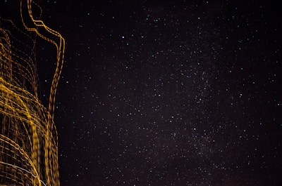 A starry night sky fills most of the image, with numerous small stars visible against the dark background. On the left, streaks of golden light create abstract patterns, suggesting motion or long exposure photography.