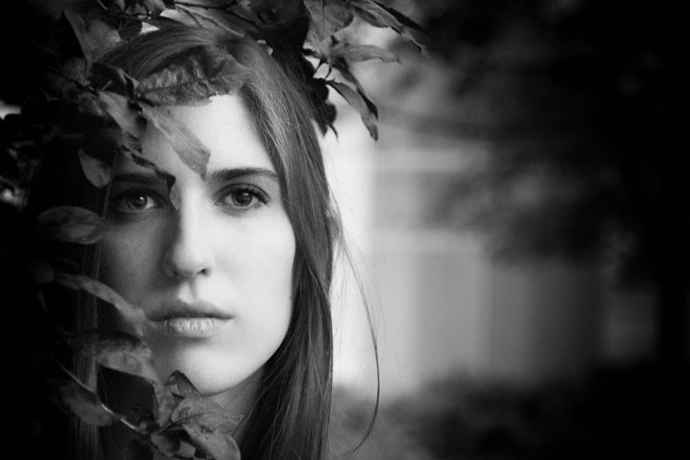 grayscale photo of woman beside leaves