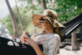woman lying on black hammock while holding phone